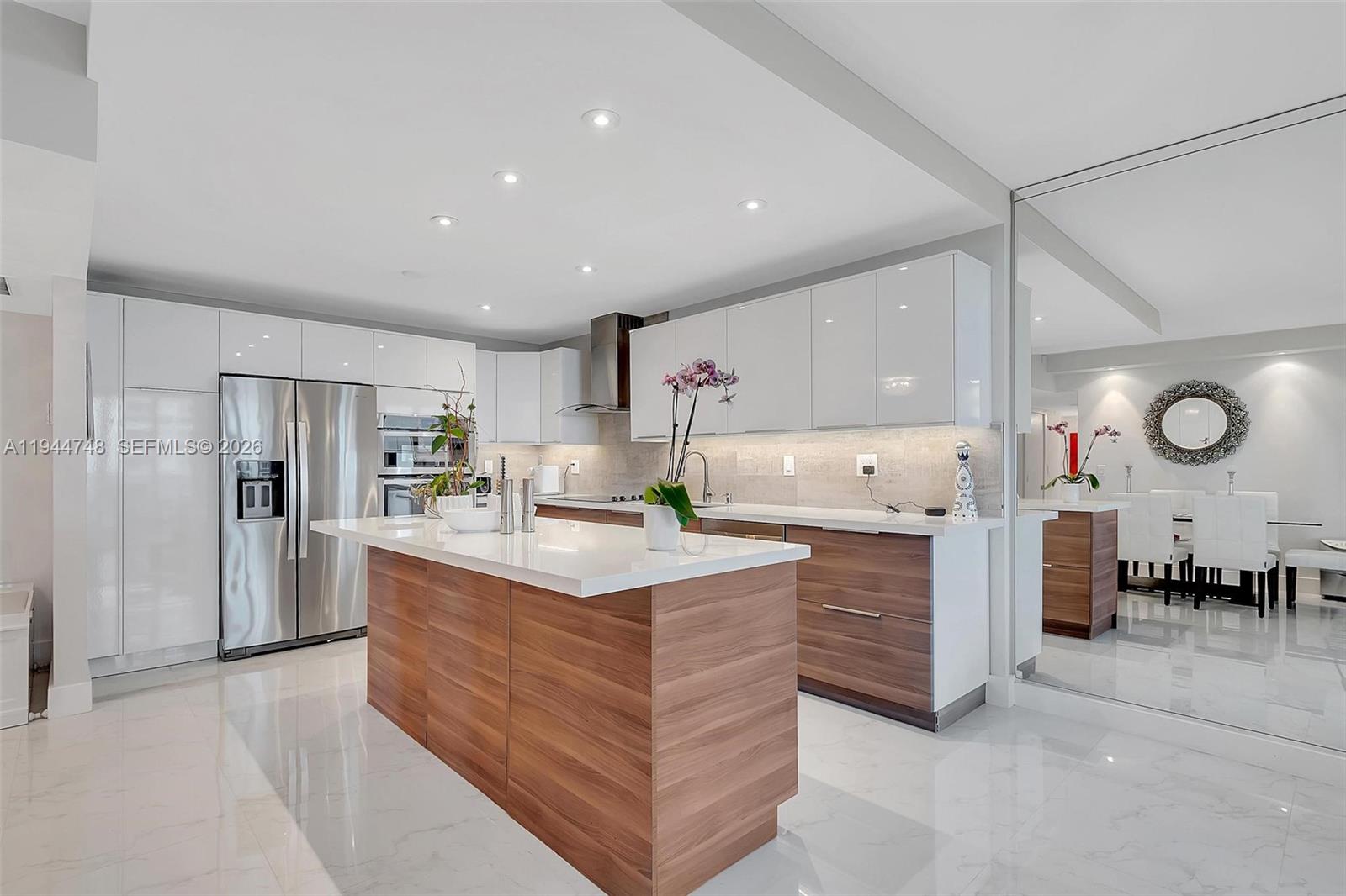 A modern kitchen features a wood-paneled island, white cabinetry, and polished tile flooring — 2301 Collins Ave # 810, Miami Beach FL 33139, MIAMI BEACH, FL