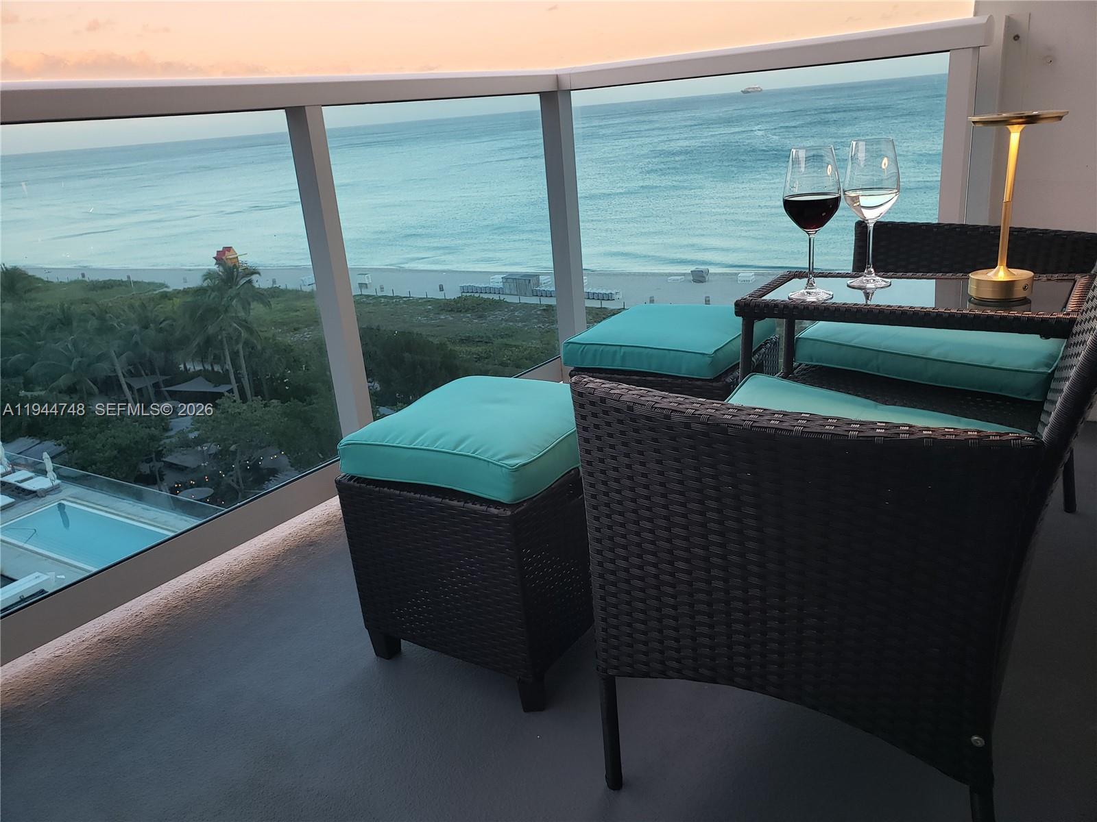 A balcony with wicker furniture and turquoise cushions overlooks the ocean at sunset — 2301 Collins Ave # 810, Miami Beach FL 33139, MIAMI BEACH, FL