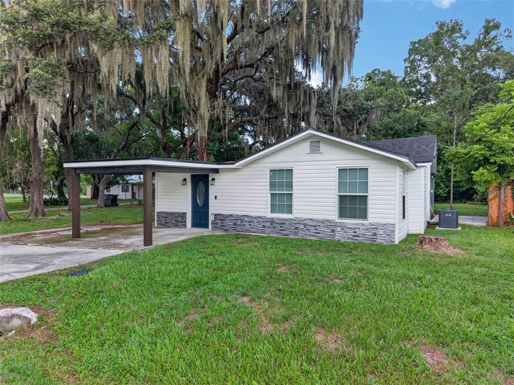 A single-story white house with a carport, stone veneer accents, and a dark blue door — 925 ADRIAN COURT, LAKELAND, FL