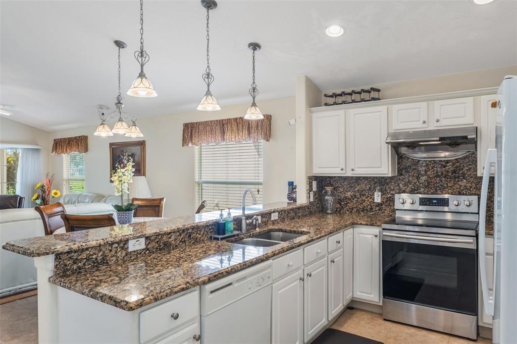 A kitchen with white cabinets, granite countertops, stainless steel appliances, and hanging pendant lights — 5389 WATERVISTA DRIVE, ORLANDO, FL