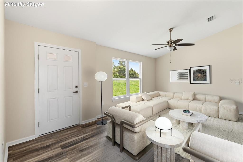 A living room with wood-look flooring, a sectional sofa, and a window overlooking a field — 2242 N NORMANDY BOULEVARD, DELTONA, FL