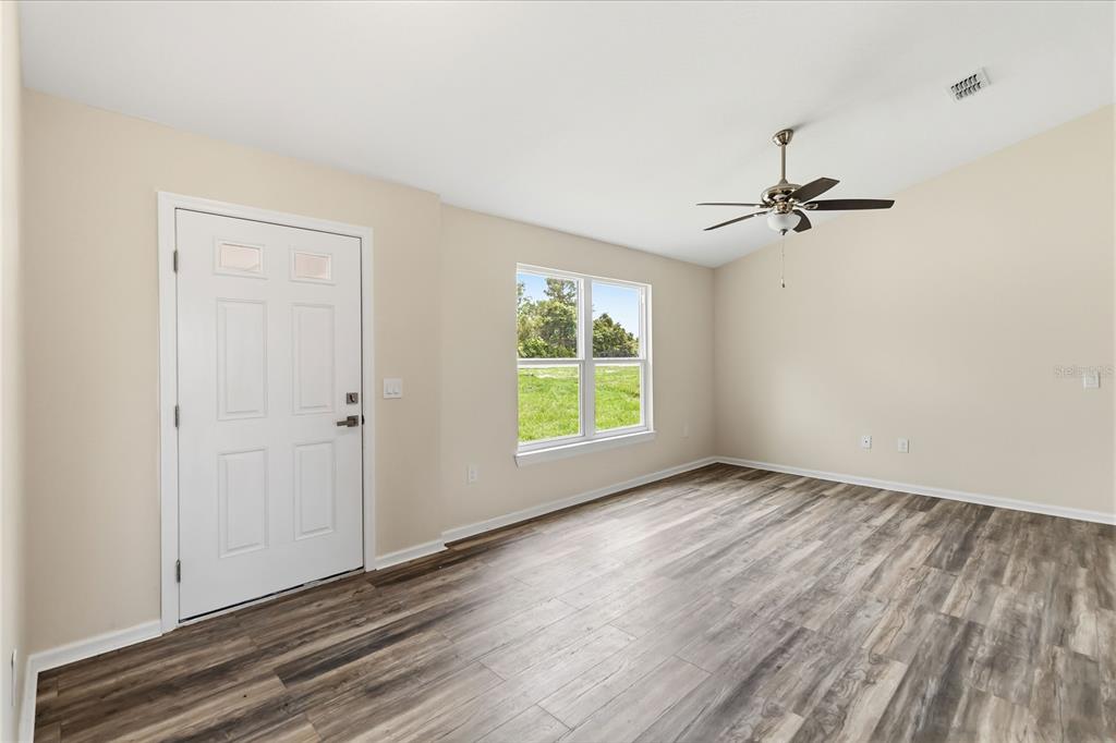 An empty room with light-colored walls, wood-look flooring, a ceiling fan, and a front door — 2242 N NORMANDY BOULEVARD, DELTONA, FL