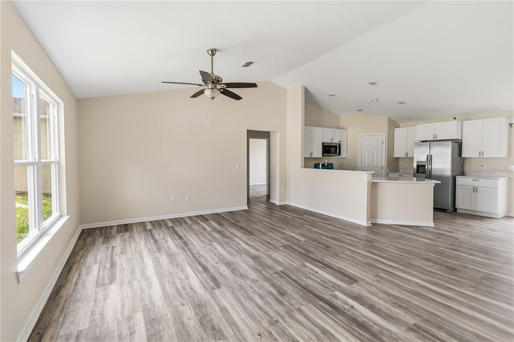 An open-concept living room features light-colored walls, wood-look flooring, a ceiling fan, and a kitchen — 2242 N NORMANDY BOULEVARD, DELTONA, FL