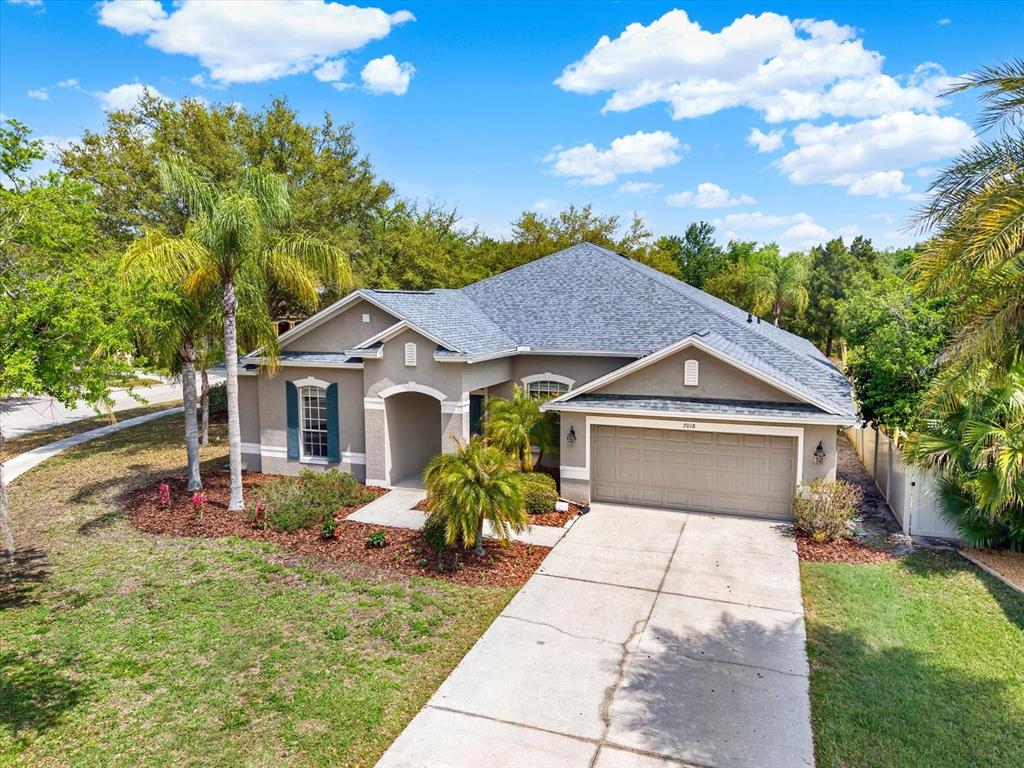 A single-story suburban house with a gray roof, tan stucco exterior, and a two-car garage — 7018 CARDINALWOOD LANE, LAND O LAKES, FL
