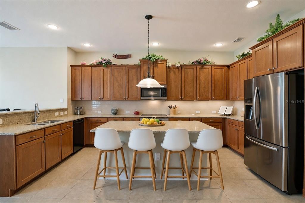 A kitchen with wood cabinets, granite countertops, a central island with stools, and stainless appliances — 7018 CARDINALWOOD LANE, LAND O LAKES, FL