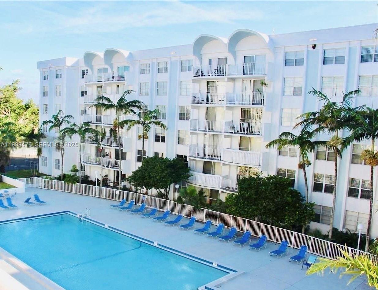 A multi-story white apartment building overlooks a rectangular swimming pool with blue lounge chairs — 494 NW 165th St Rd # 601, Miami FL 33169, MIAMI, FL