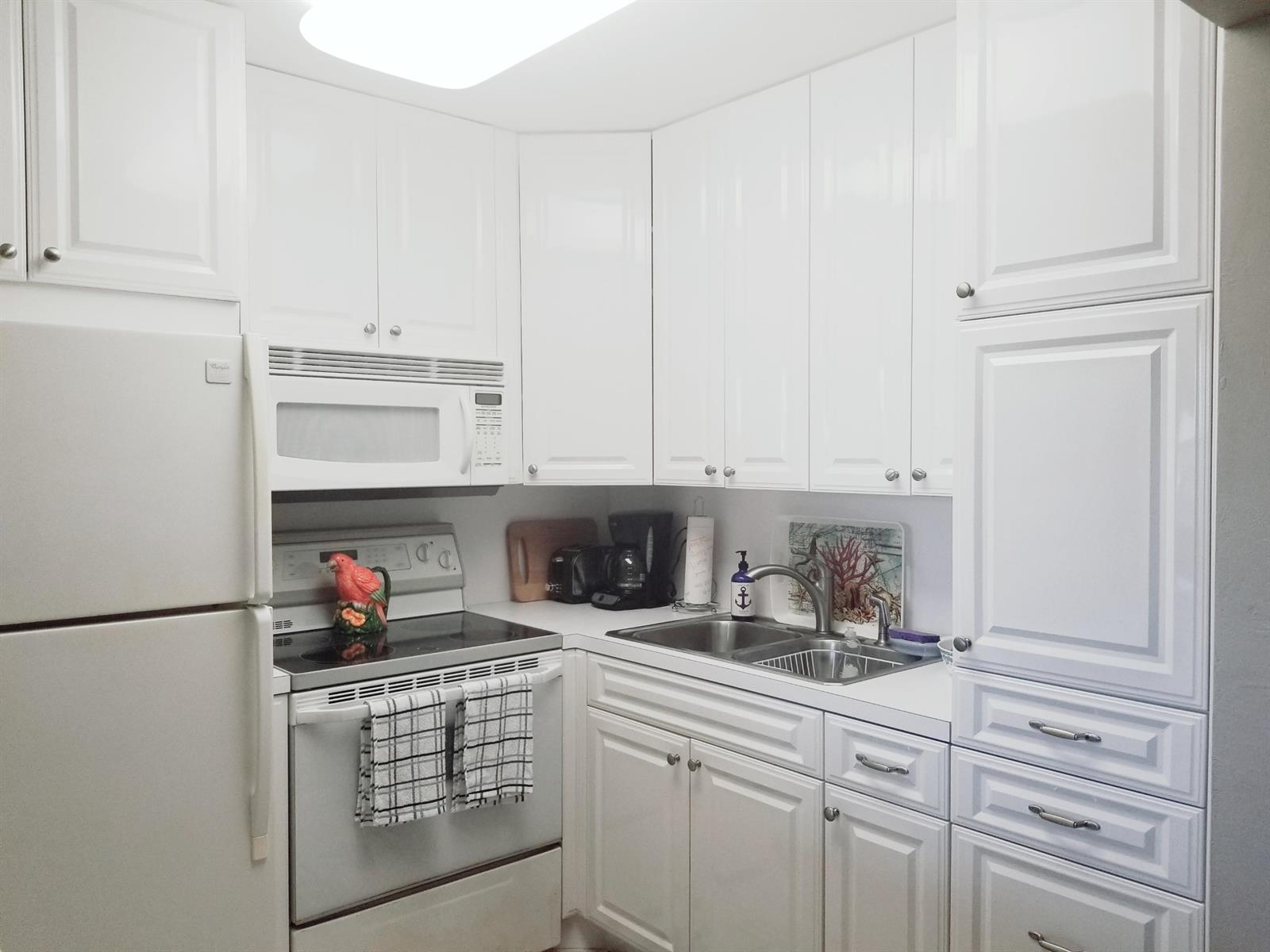 A small kitchen features white cabinets, white appliances, and a double stainless steel sink — 850 E Horizons # 207, Boynton Beach FL 33435, BOYNTON BEACH, FL