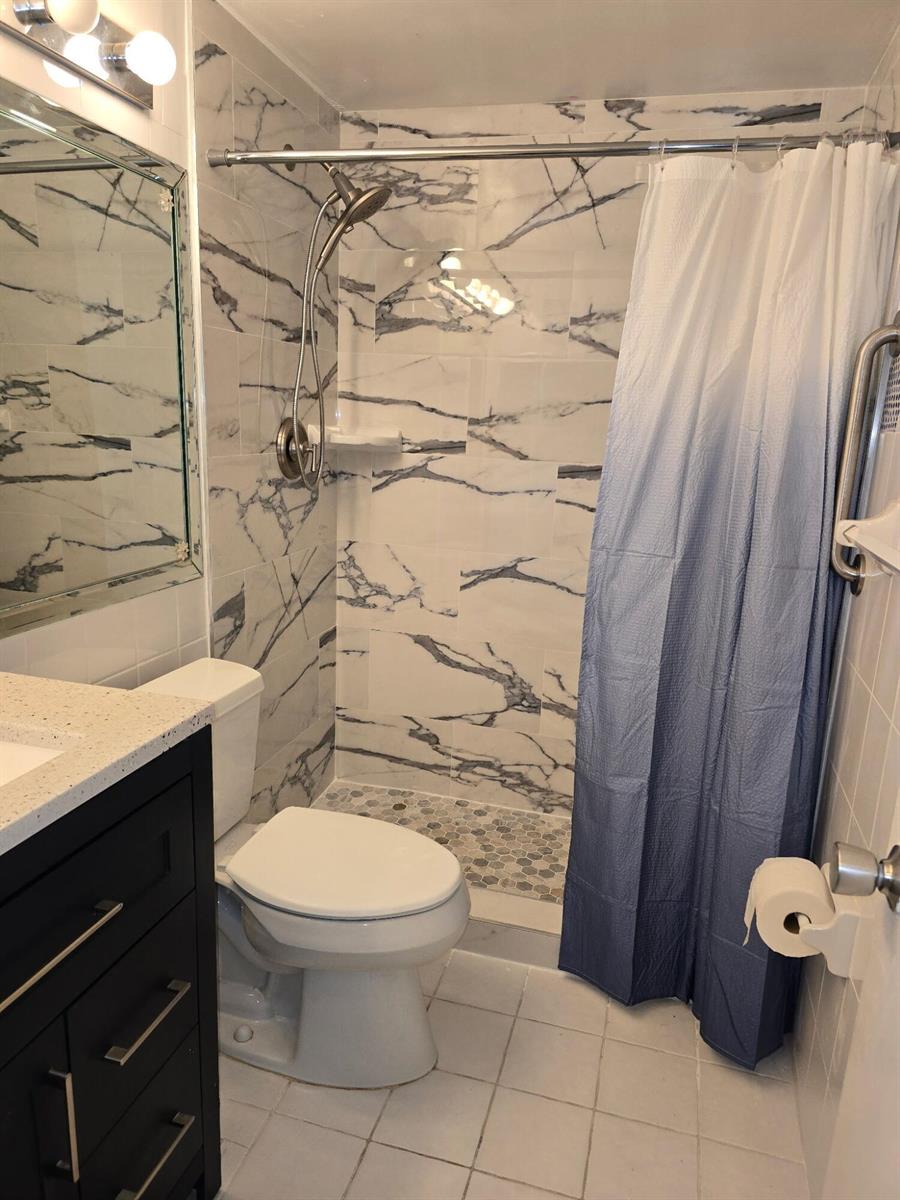 A bathroom features a marble-tiled shower with a blue ombre curtain and a dark vanity — 850 E Horizons # 207, Boynton Beach FL 33435, BOYNTON BEACH, FL