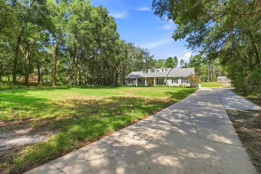 A single-story house with a concrete driveway sits on a large, grassy, tree-lined lot — 20257 SW 97TH PLACE, DUNNELLON, FL
