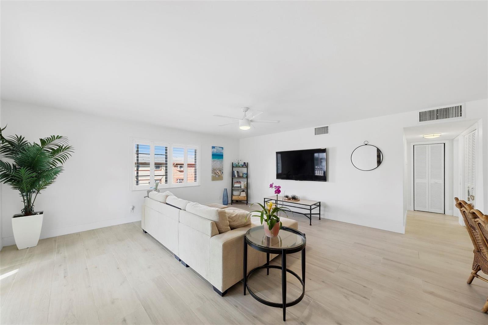 A bright living room features a beige sectional sofa, a wall-mounted television, and light flooring — 1450 N Riverside Drive # 201, Pompano Beach FL 33062, POMPANO BEACH, FL