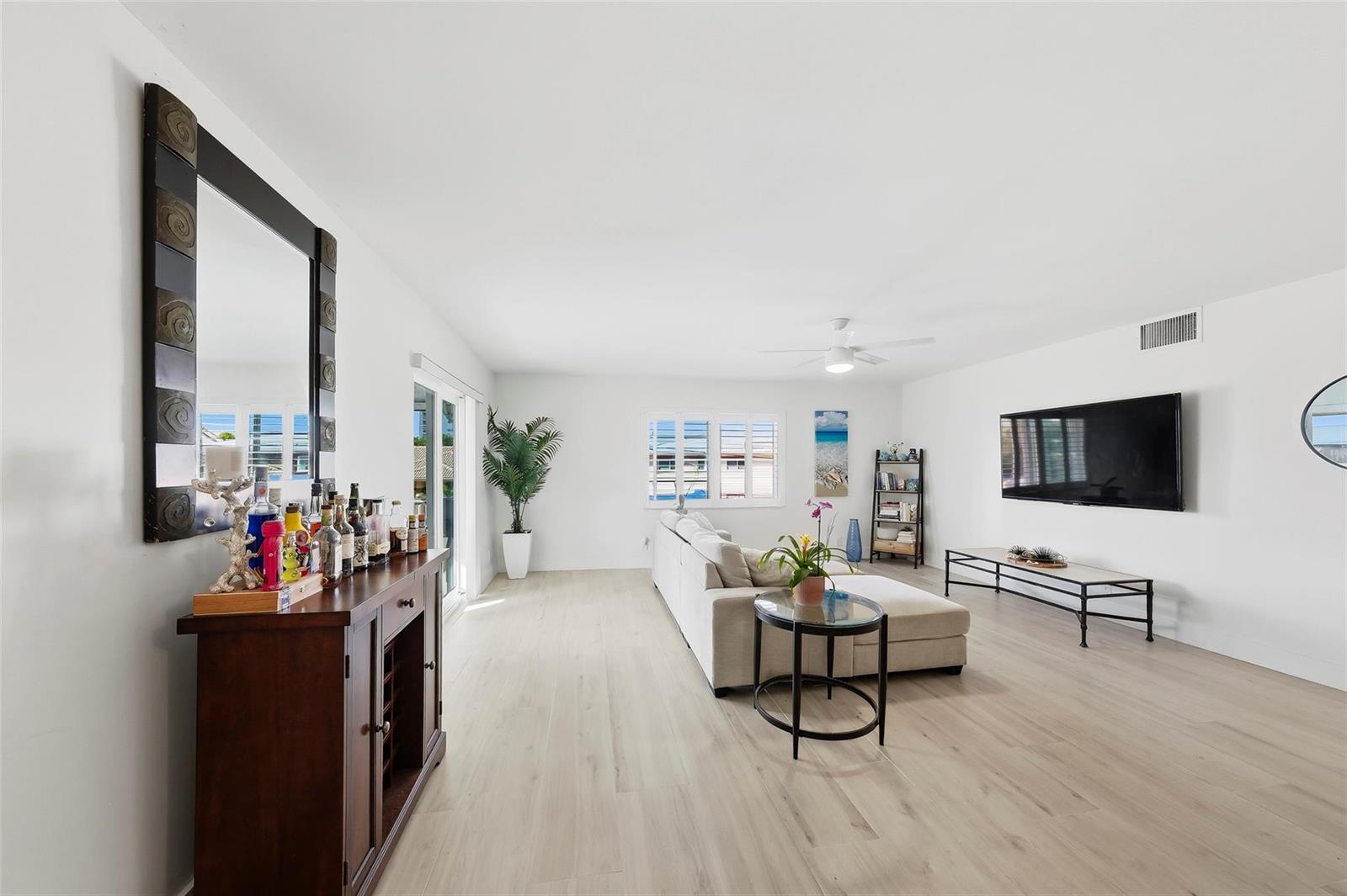 A living room features light wood-look flooring, a sectional sofa, and a wall-mounted television — 1450 N Riverside Drive # 201, Pompano Beach FL 33062, POMPANO BEACH, FL