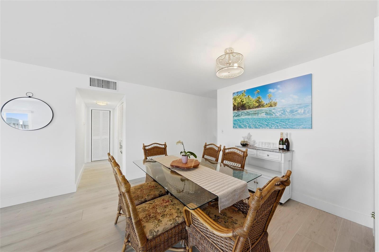 A dining room features a glass-topped table, wicker chairs, and a tropical wall art piece — 1450 N Riverside Drive # 201, Pompano Beach FL 33062, POMPANO BEACH, FL