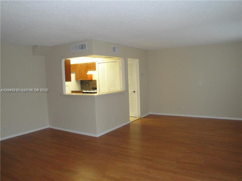 An interior view shows a living area with wood-look flooring and a kitchen pass-through window — 18111 NW 68th Ave # I208, Hialeah FL 33015, HIALEAH, FL