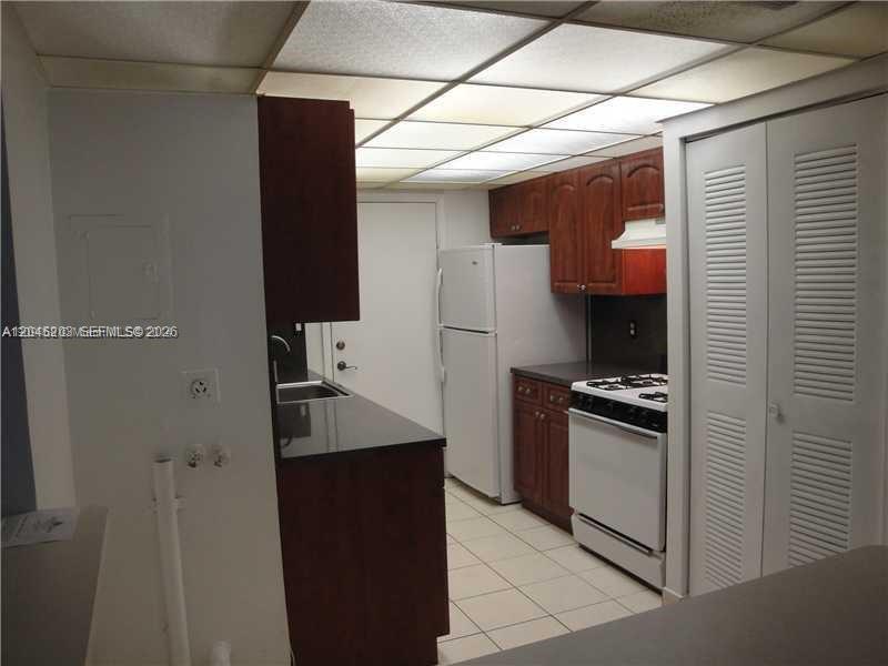 A kitchen features dark wood cabinets, white appliances, a tiled floor, and a drop ceiling — 18111 NW 68th Ave # I208, Hialeah FL 33015, HIALEAH, FL