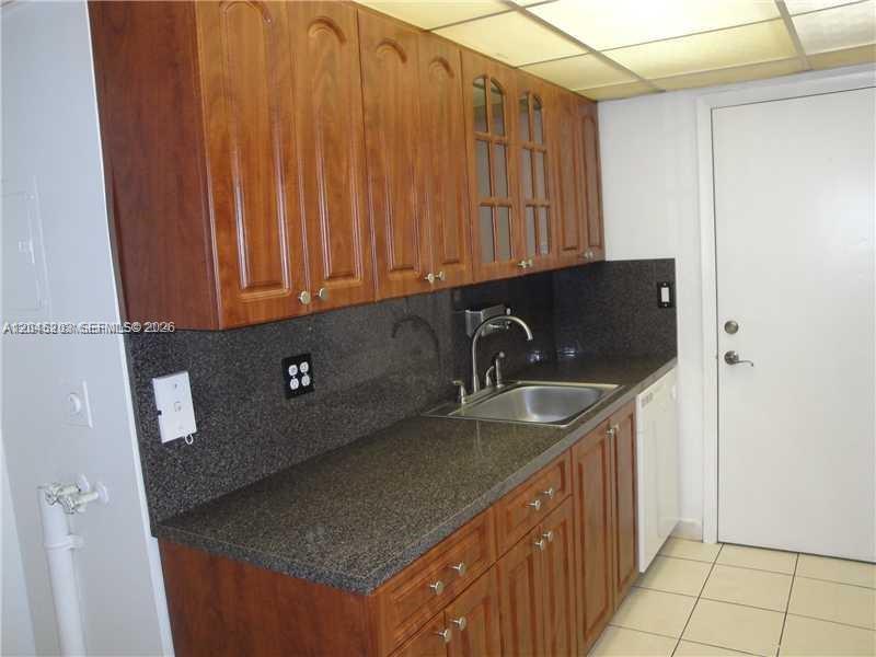 A kitchen features wood cabinets, dark granite countertops, a stainless steel sink, and tile flooring — 18111 NW 68th Ave # I208, Hialeah FL 33015, HIALEAH, FL