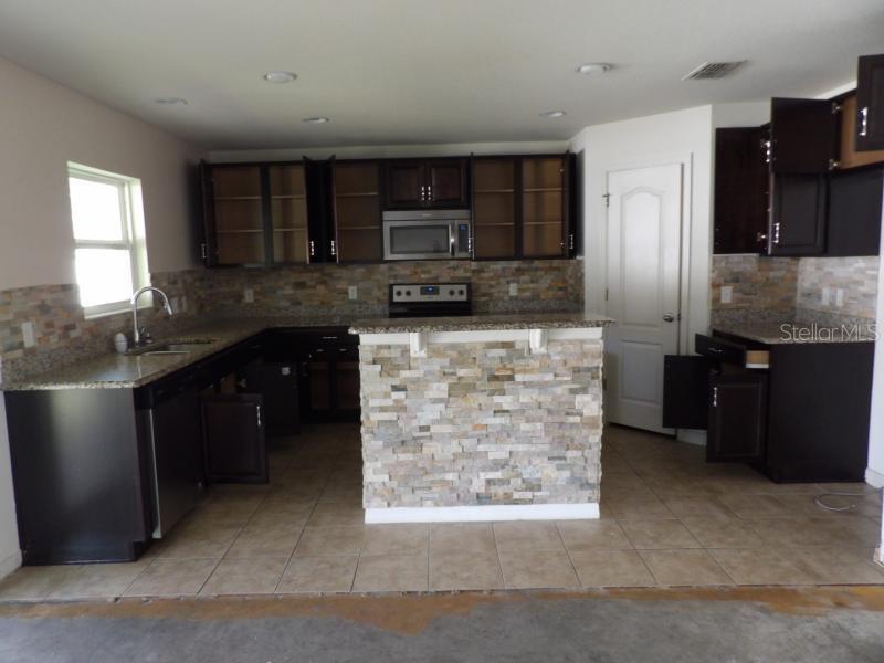 A kitchen features dark wood cabinets, stone tile backsplash, granite countertops, and a stone-faced island — 11301 BRIGHTON KNOLL LOOP, RIVERVIEW, FL