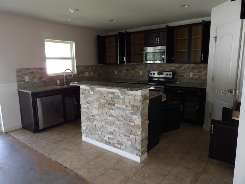 A kitchen with dark cabinets, granite countertops, a stone-faced island, and stainless steel appliances — 11301 BRIGHTON KNOLL LOOP, RIVERVIEW, FL