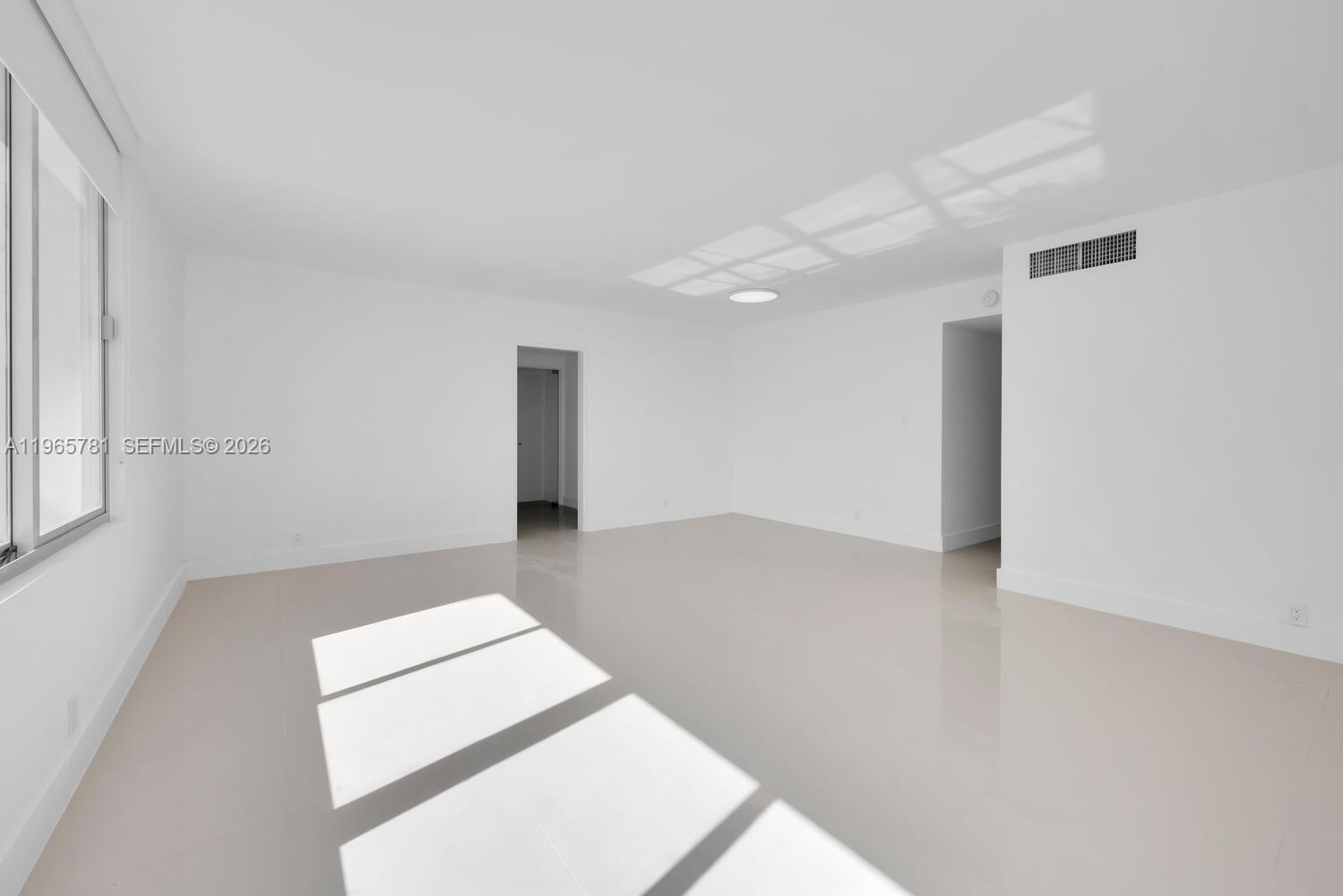 An empty, white-walled room features large windows, glossy tile flooring, and two doorways — 1000 West Ave # 301, Miami Beach FL 33139, MIAMI BEACH, FL