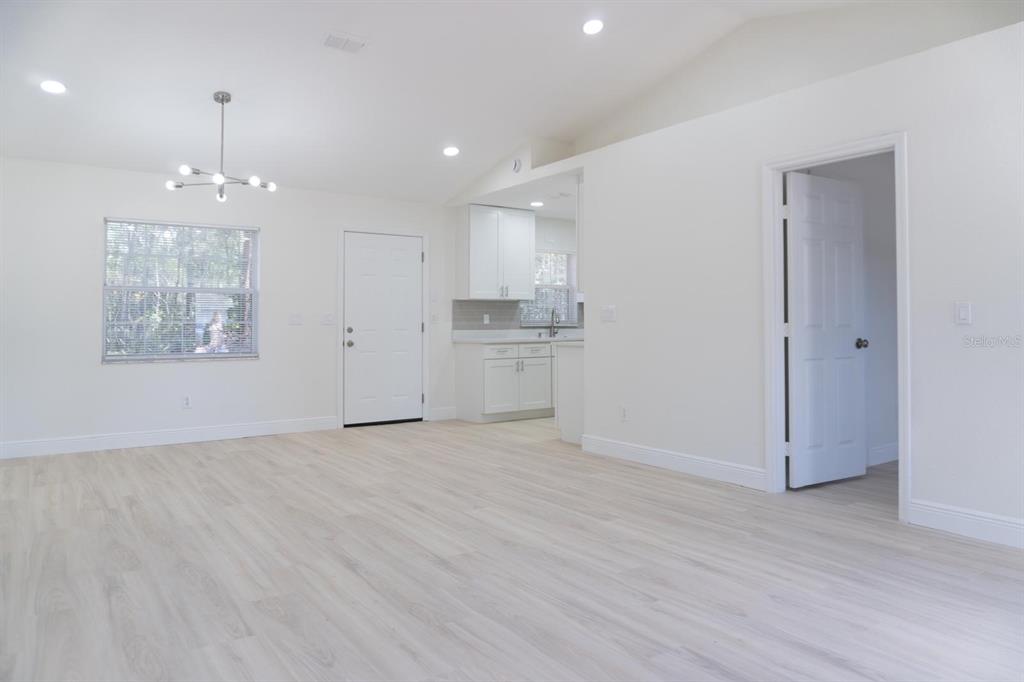 A bright, open-concept living area features light wood-look flooring, white walls, and a modern chandelier — 5701 NW 59TH COURT, OCALA, FL