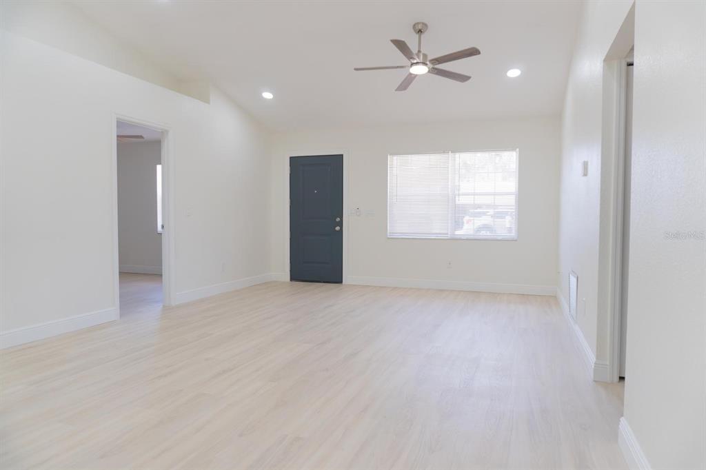 A bright living room features light wood-look flooring, white walls, a ceiling fan, and a door — 5701 NW 59TH COURT, OCALA, FL