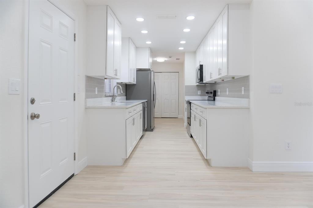 A galley kitchen features white cabinets, light countertops, stainless steel appliances, and light wood flooring — 5701 NW 59TH COURT, OCALA, FL