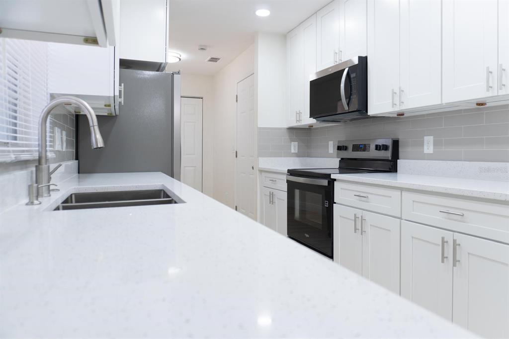 A modern kitchen features white cabinets, quartz countertops, stainless steel appliances, and a gray backsplash — 5701 NW 59TH COURT, OCALA, FL
