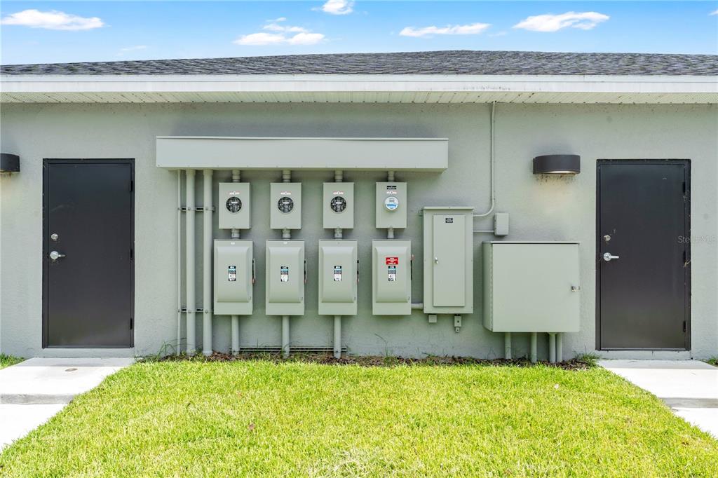 An exterior view of a building wall featuring multiple electrical meters and utility boxes — 600 LEXINGTON GREEN LANE, SANFORD, FL