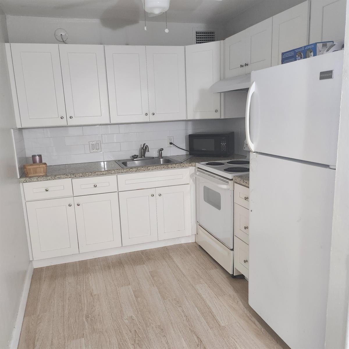 A small kitchen features white cabinets, granite countertops, a white stove, and a white refrigerator — 643 Durham W, Deerfield Beach FL 33442, DEERFIELD BEACH, FL