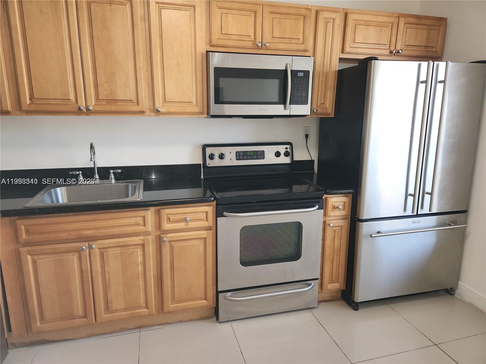 A kitchen features light wood cabinets, black countertops, and stainless steel appliances — 8059 SW 21 CT # 8059, Miramar FL 33025, MIRAMAR, FL