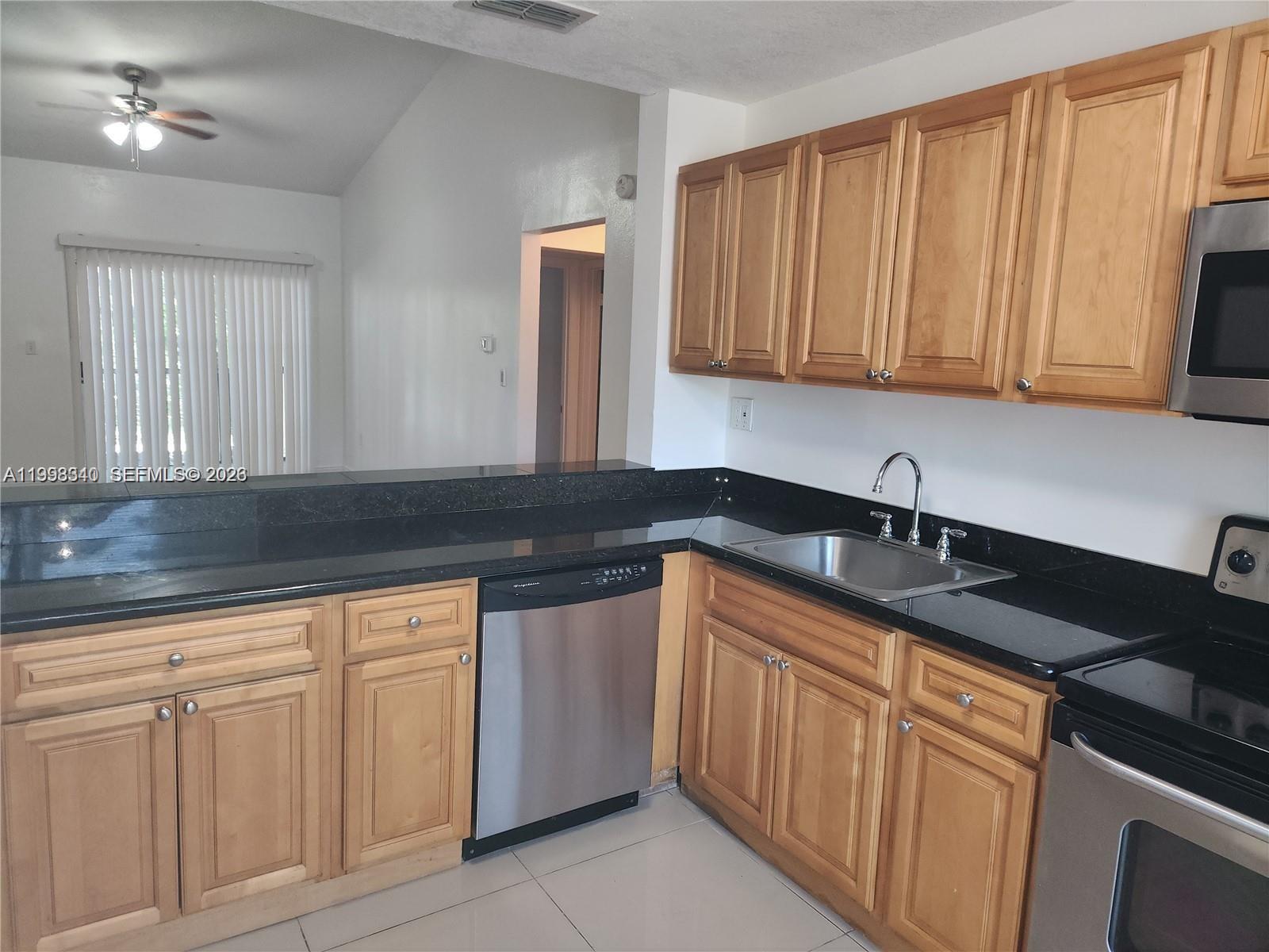 A kitchen features light wood cabinets, black granite countertops, and stainless steel appliances — 8059 SW 21 CT # 8059, Miramar FL 33025, MIRAMAR, FL