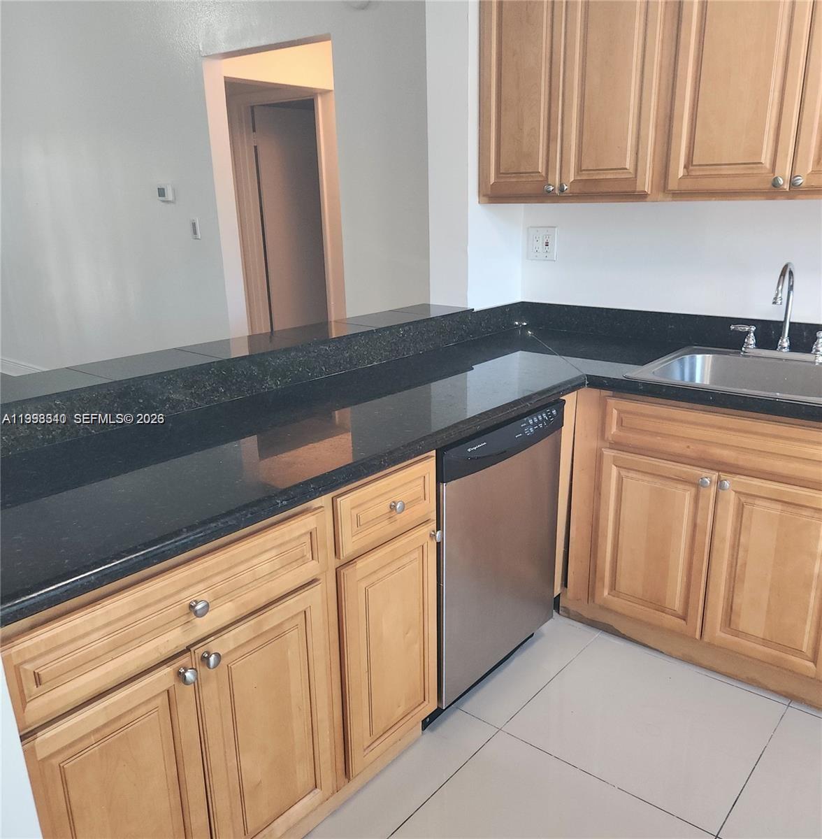 A kitchen features light wood cabinets, black granite countertops, and a stainless steel dishwasher — 8059 SW 21 CT # 8059, Miramar FL 33025, MIRAMAR, FL