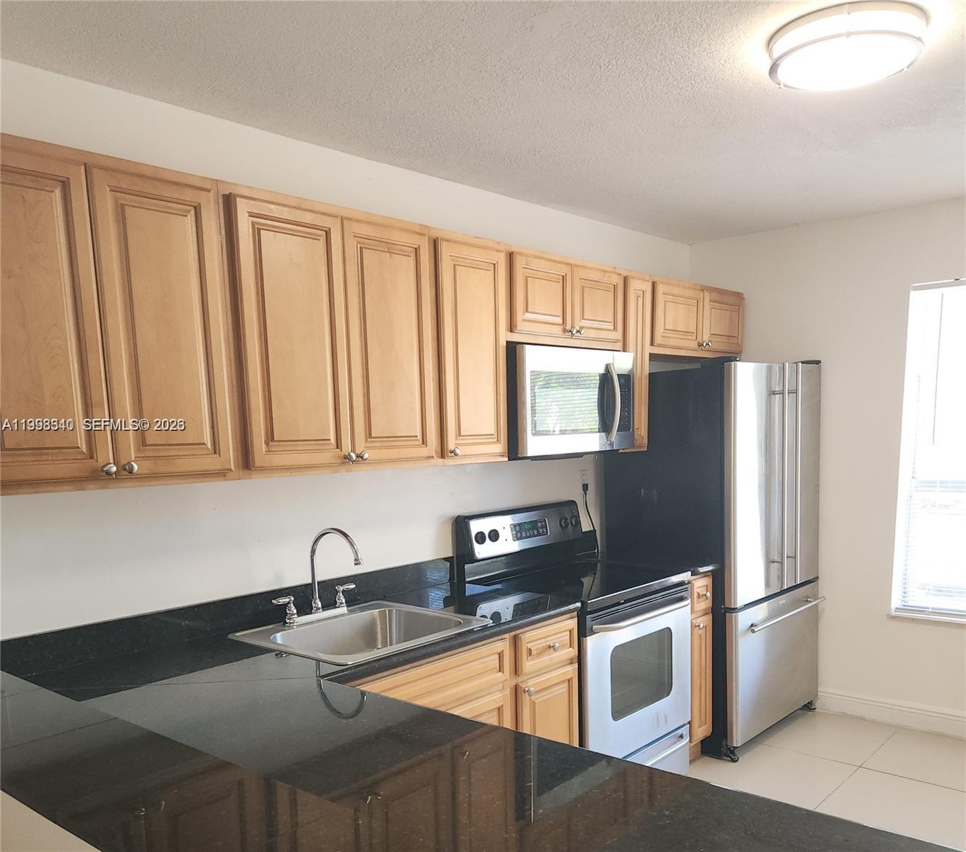 A kitchen features light wood cabinets, black countertops, and stainless steel appliances — 8059 SW 21 CT # 8059, Miramar FL 33025, MIRAMAR, FL