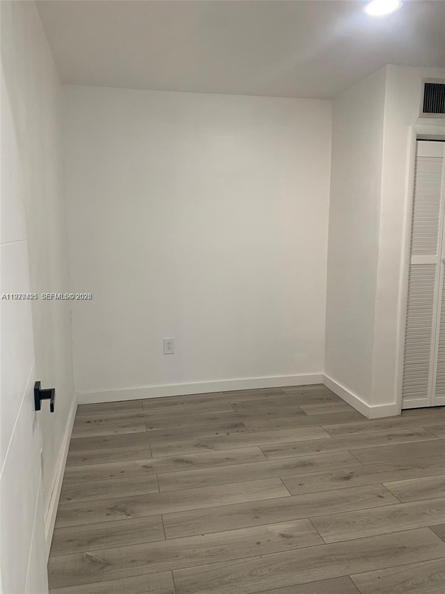 An empty room features white walls, light wood-look flooring, and a white louvered closet door — 8295 NE Miami Ct # 1, Miami FL 33138, MIAMI, FL