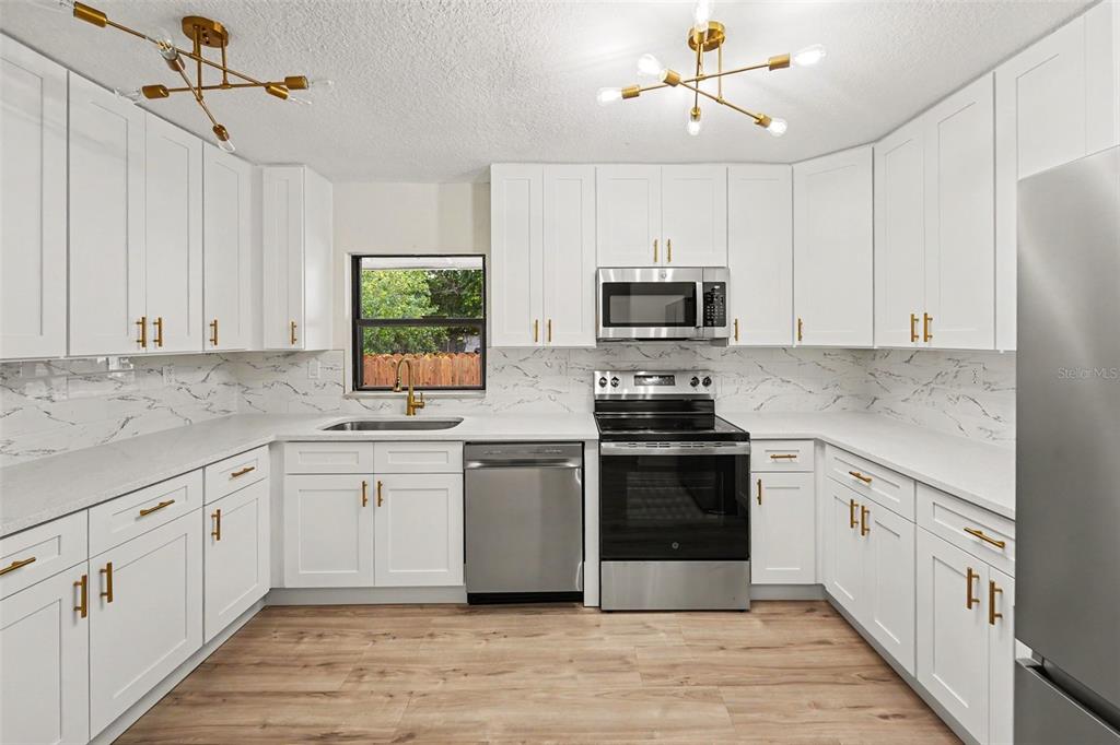A kitchen features white cabinets, stainless steel appliances, marble-look countertops, and two modern light fixtures — 2850 59TH AVENUE N, ST PETERSBURG, FL