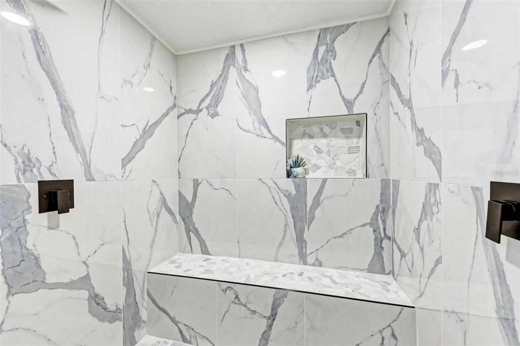 A walk-in shower features white marble-look wall tiles, a built-in bench, and dark fixtures — 3120 GUADALUPE DRIVE, PUNTA GORDA, FL