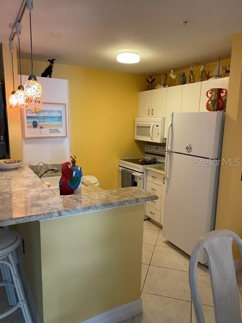A kitchen features yellow walls, white cabinets, a white refrigerator, and a granite-topped breakfast bar — 850 S TAMIAMI TRAIL UNIT 130, SARASOTA, FL