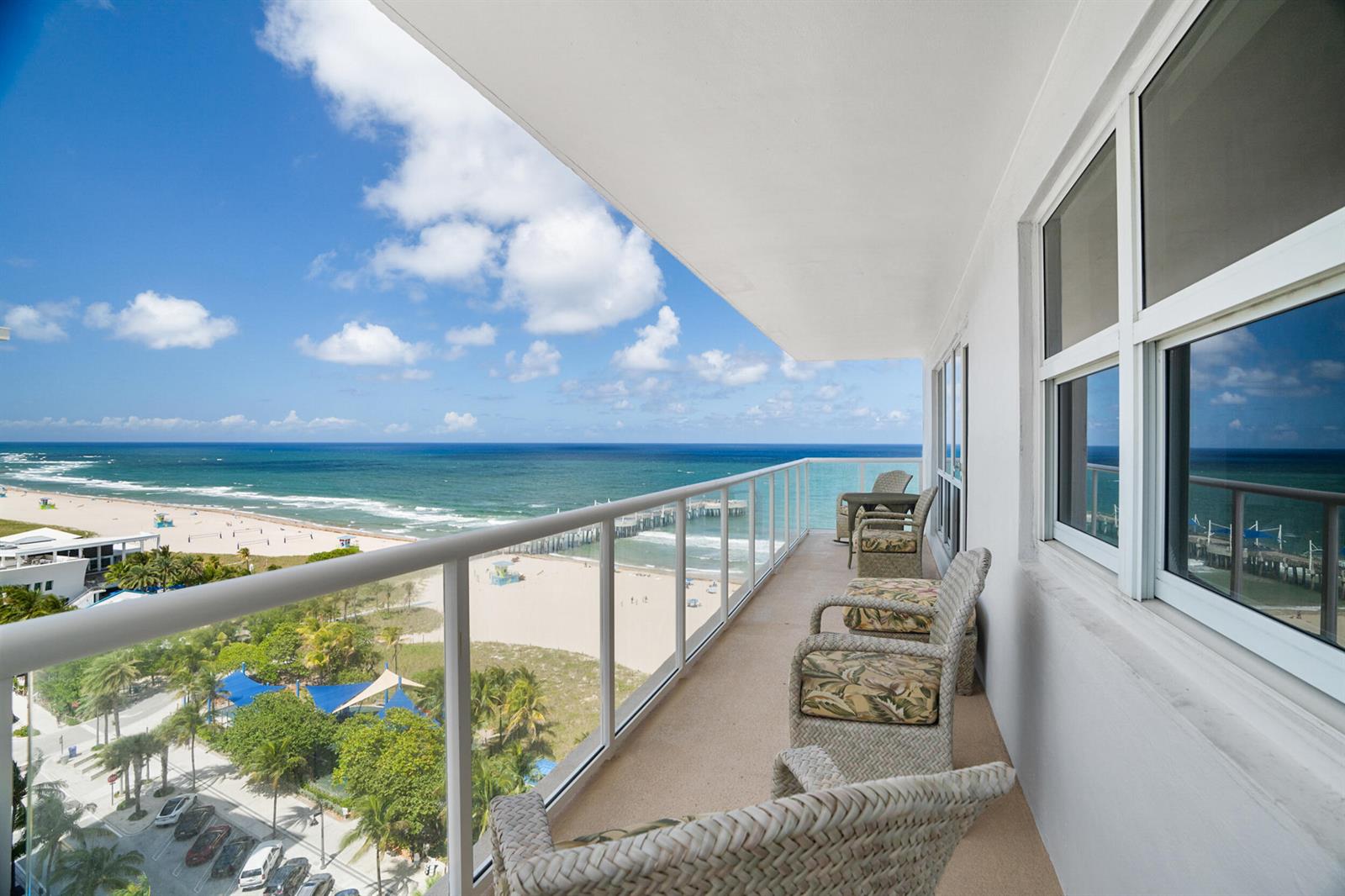 A balcony with wicker chairs overlooks a sandy beach, ocean, and a pier — 111 N Pompano Beach Boulevard # 1609, Pompano Beach FL 33062, POMPANO BEACH, FL