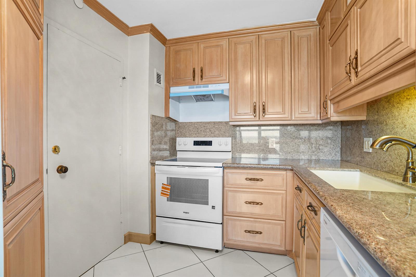 A kitchen features light wood cabinets, granite countertops, a white stove, and white tile floors — 111 N Pompano Beach Boulevard # 1609, Pompano Beach FL 33062, POMPANO BEACH, FL