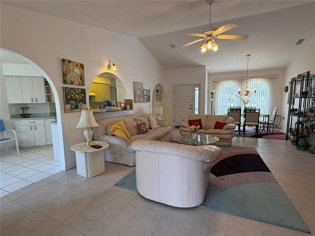 A living room with tile floors, vaulted ceilings, a ceiling fan, and an arched kitchen pass-through — 21498 BEAVERTON AVENUE, PORT CHARLOTTE, FL