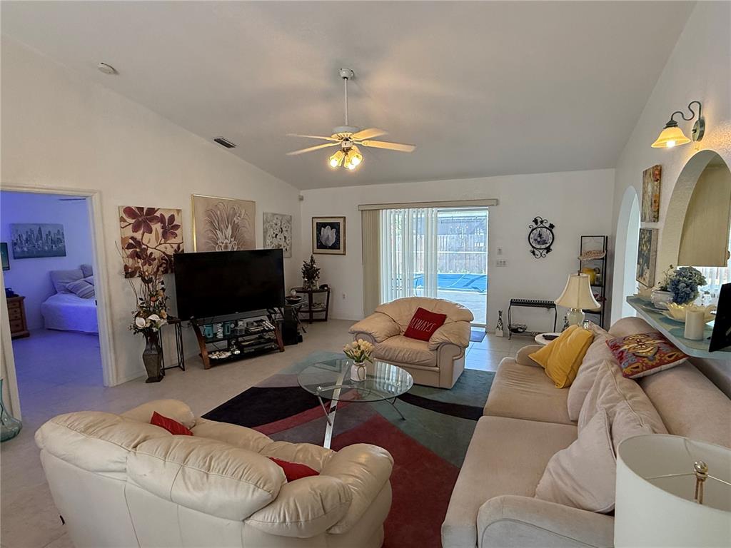 A living room features a vaulted ceiling, a ceiling fan, a television, and tiled floors — 21498 BEAVERTON AVENUE, PORT CHARLOTTE, FL