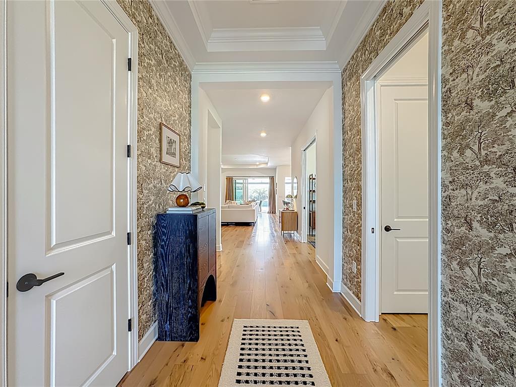 A hallway with patterned wallpaper, hardwood floors, and a dark blue cabinet leads to a living area — 16306 ISOLA PL, LAKEWOOD RANCH, FL