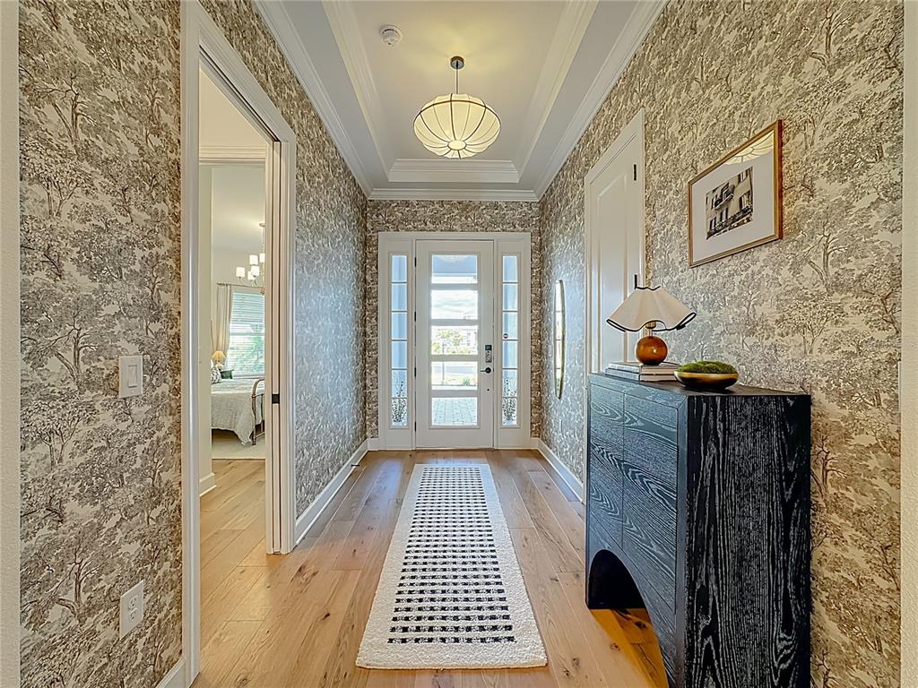 A foyer features patterned wallpaper, a black console table, a runner rug, and a tray ceiling — 16306 ISOLA PL, LAKEWOOD RANCH, FL