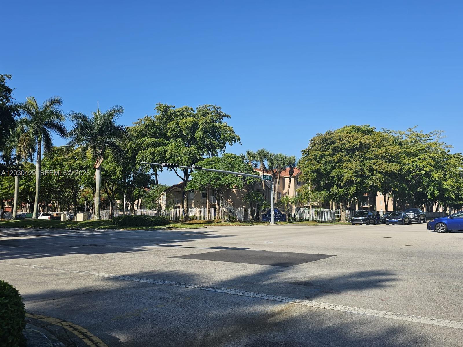 An intersection with palm trees, mature greenery, and multi-story apartment buildings under a clear sky — 15771 SW 106th Ter # 204, Miami FL 33196, MIAMI, FL