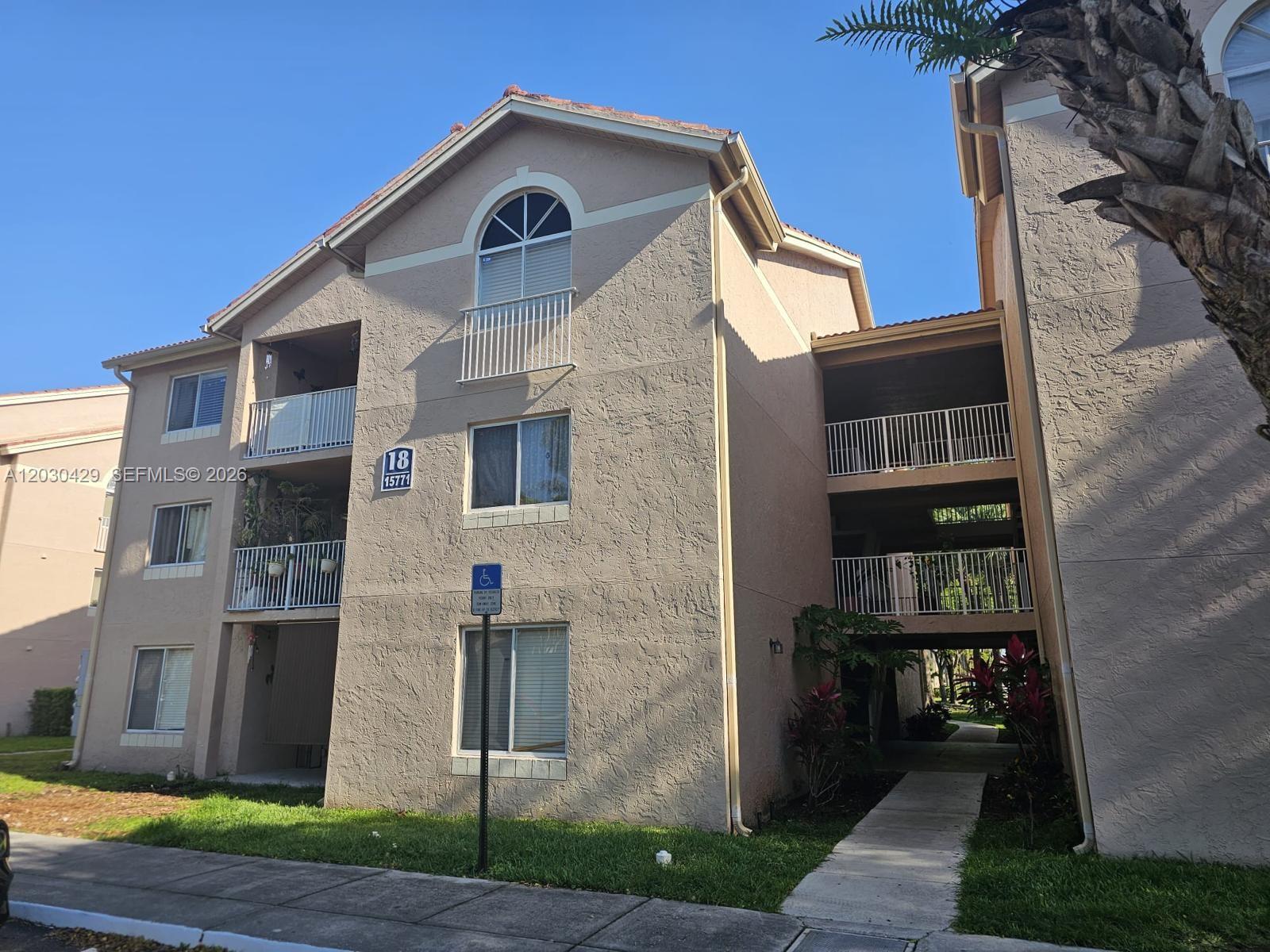 A three-story beige stucco apartment building features balconies and a walkway between two sections — 15771 SW 106th Ter # 204, Miami FL 33196, MIAMI, FL