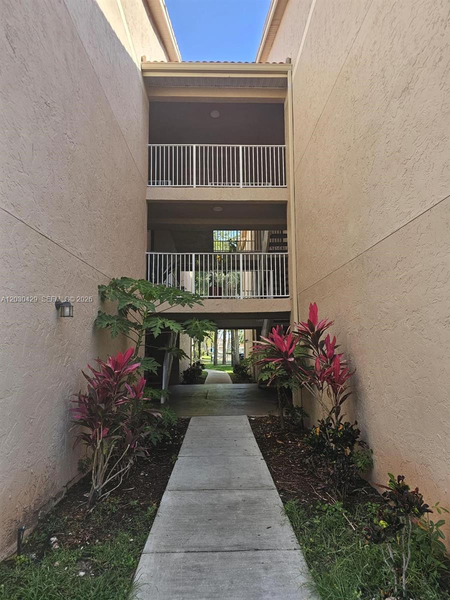 A concrete walkway leads between two beige apartment buildings toward a landscaped courtyard — 15771 SW 106th Ter # 204, Miami FL 33196, MIAMI, FL