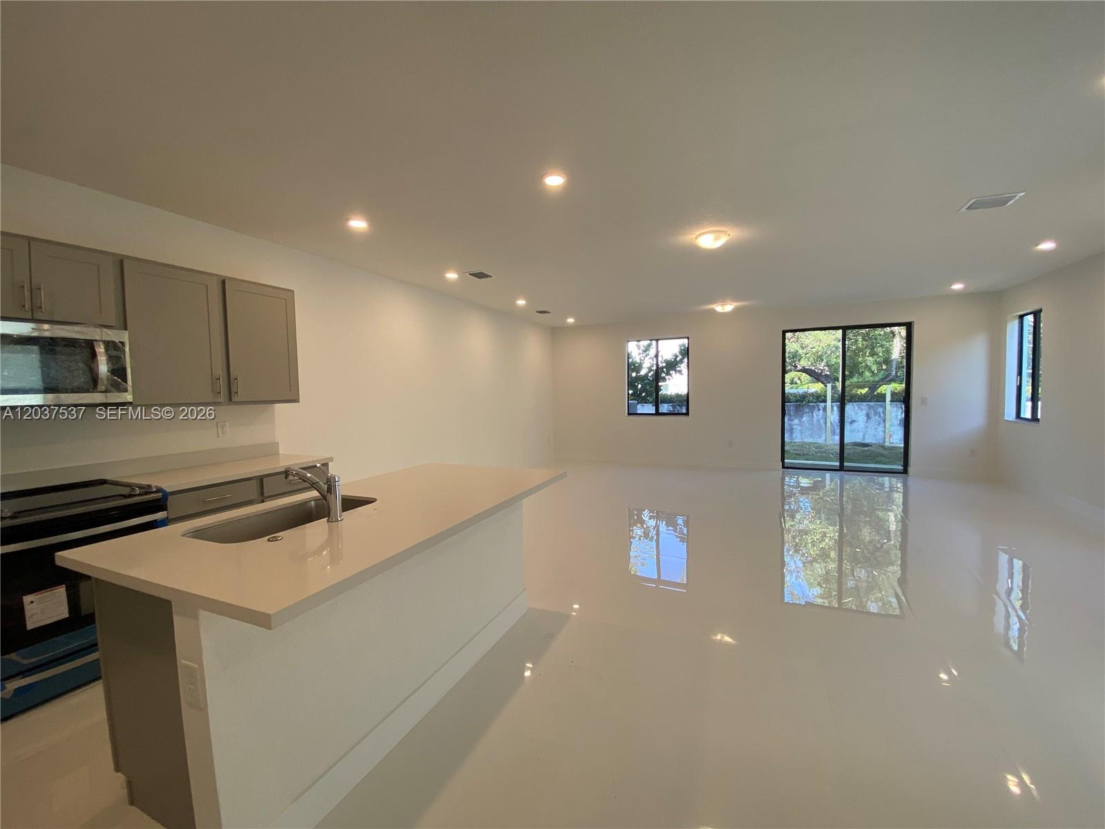 A modern kitchen with gray cabinets and a white island overlooks an open living area — 2402 SW 145th Pl # 0, Miami FL 33175, MIAMI, FL