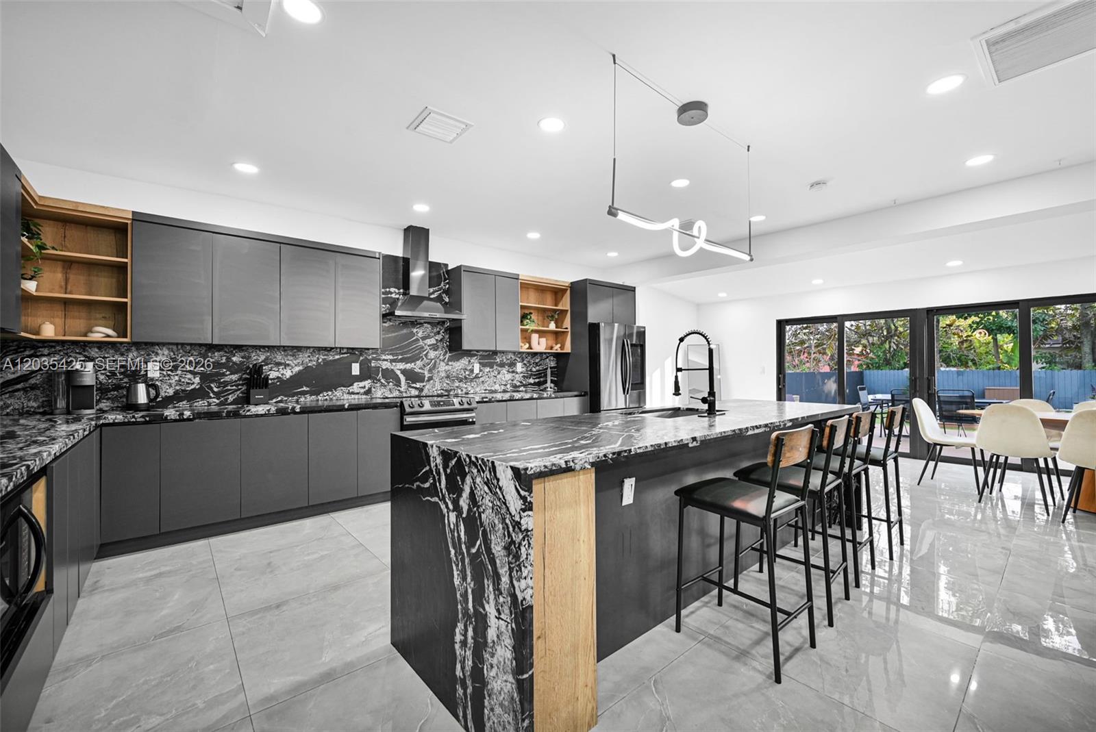 A modern kitchen features dark gray cabinetry, black marble countertops, and a large matching island — 112 NW 53rd St # 112, Miami FL 33127, MIAMI, FL