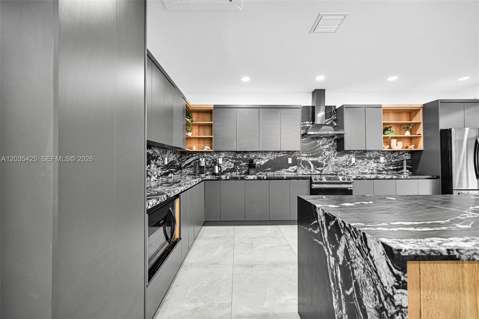 A modern kitchen features dark gray cabinetry, black marble countertops, and light wood shelving — 112 NW 53rd St # 112, Miami FL 33127, MIAMI, FL