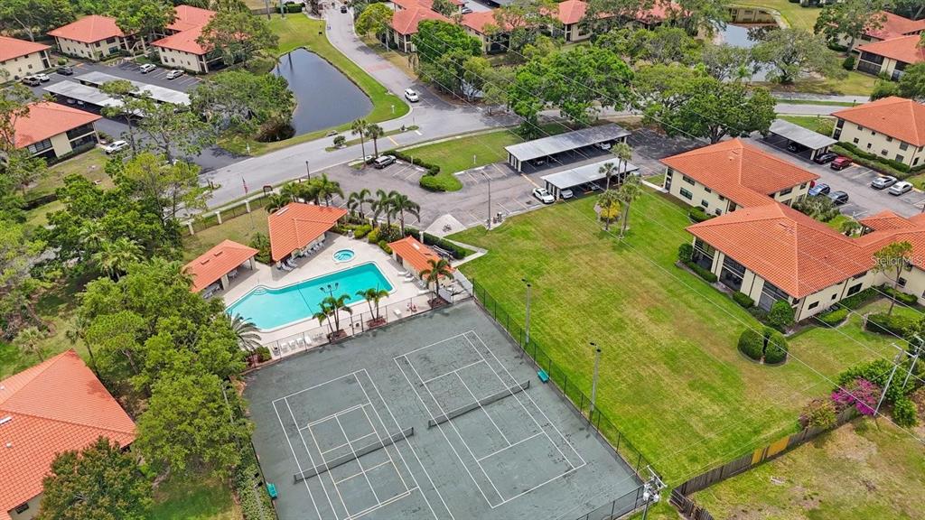 An aerial view shows a community pool, tennis courts, and multi-family residential buildings with parking — 404 HAMMOCK PINE BOULEVARD UNIT 404, CLEARWATER, FL