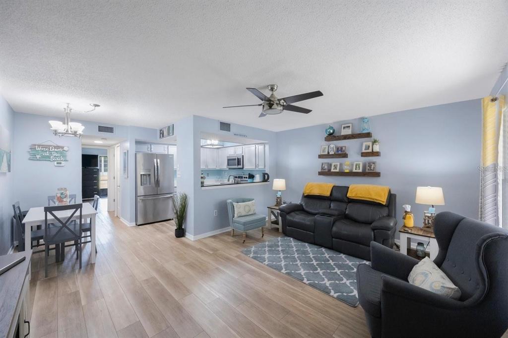 A living room and dining area with light wood floors, a black sofa, and kitchen pass-through — 404 HAMMOCK PINE BOULEVARD UNIT 404, CLEARWATER, FL